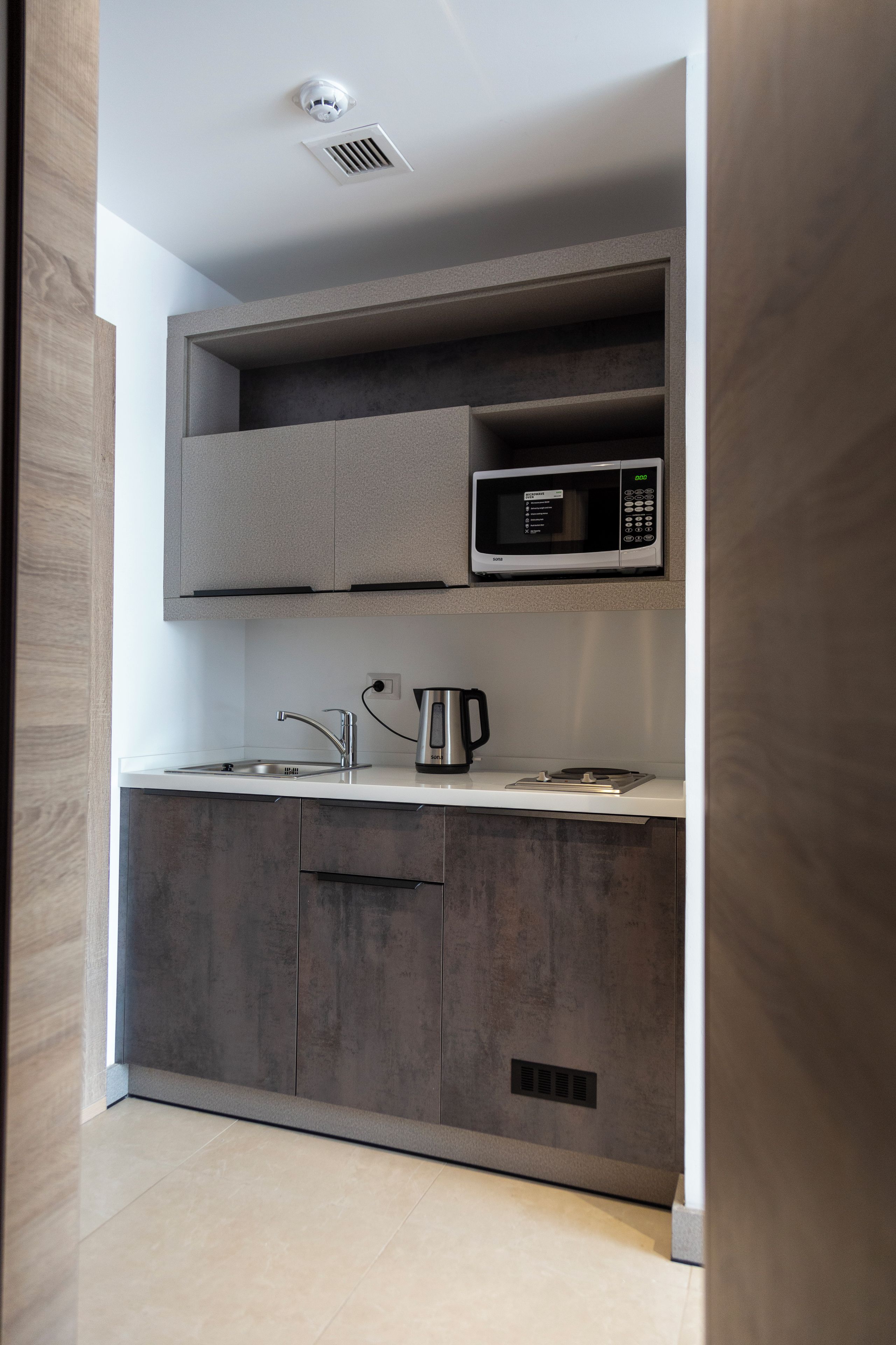 A modern kitchen with grey cabinets, a microwave, a kettle, and a sink.