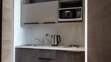 A modern kitchen with grey cabinets, a microwave, a kettle, and a sink.