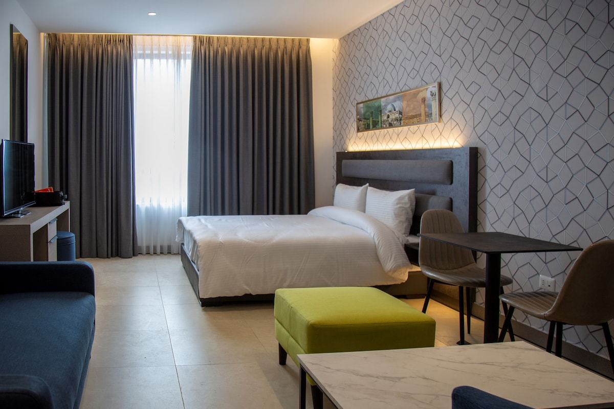 A hotel room with a bed, a desk with a computer, a dining table, and a sofa.