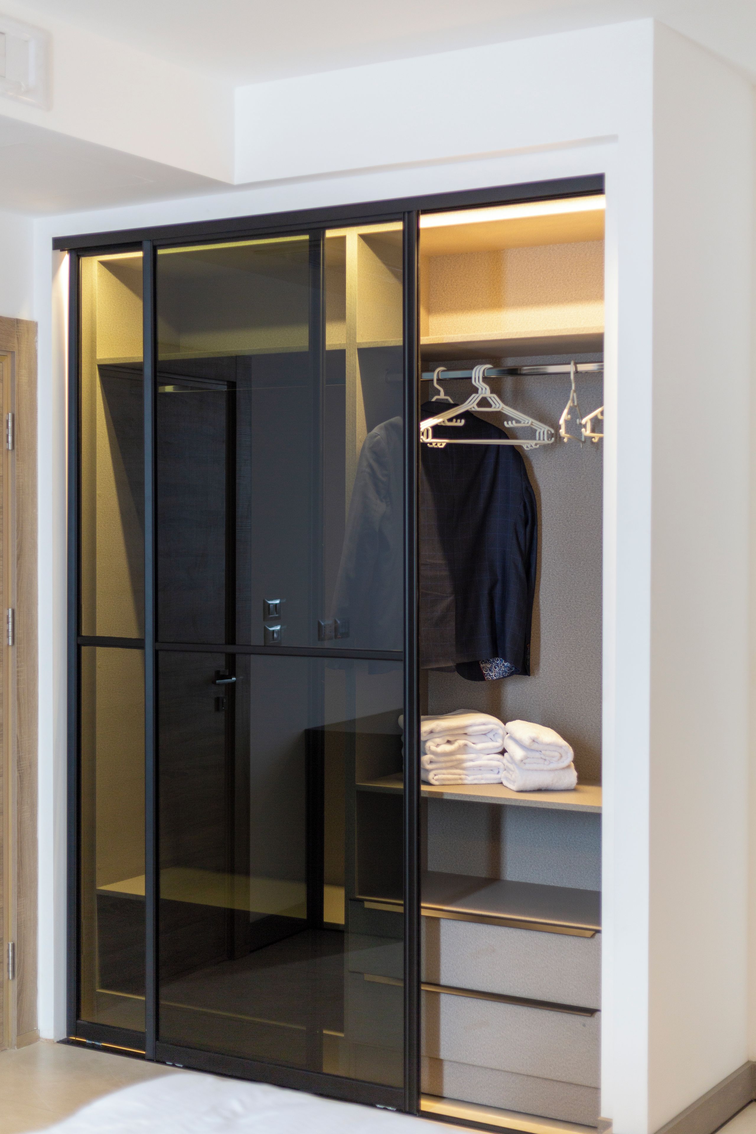 A modern walk-in closet with a mirrored wardrobe, a hanging rack, and neatly folded towels.