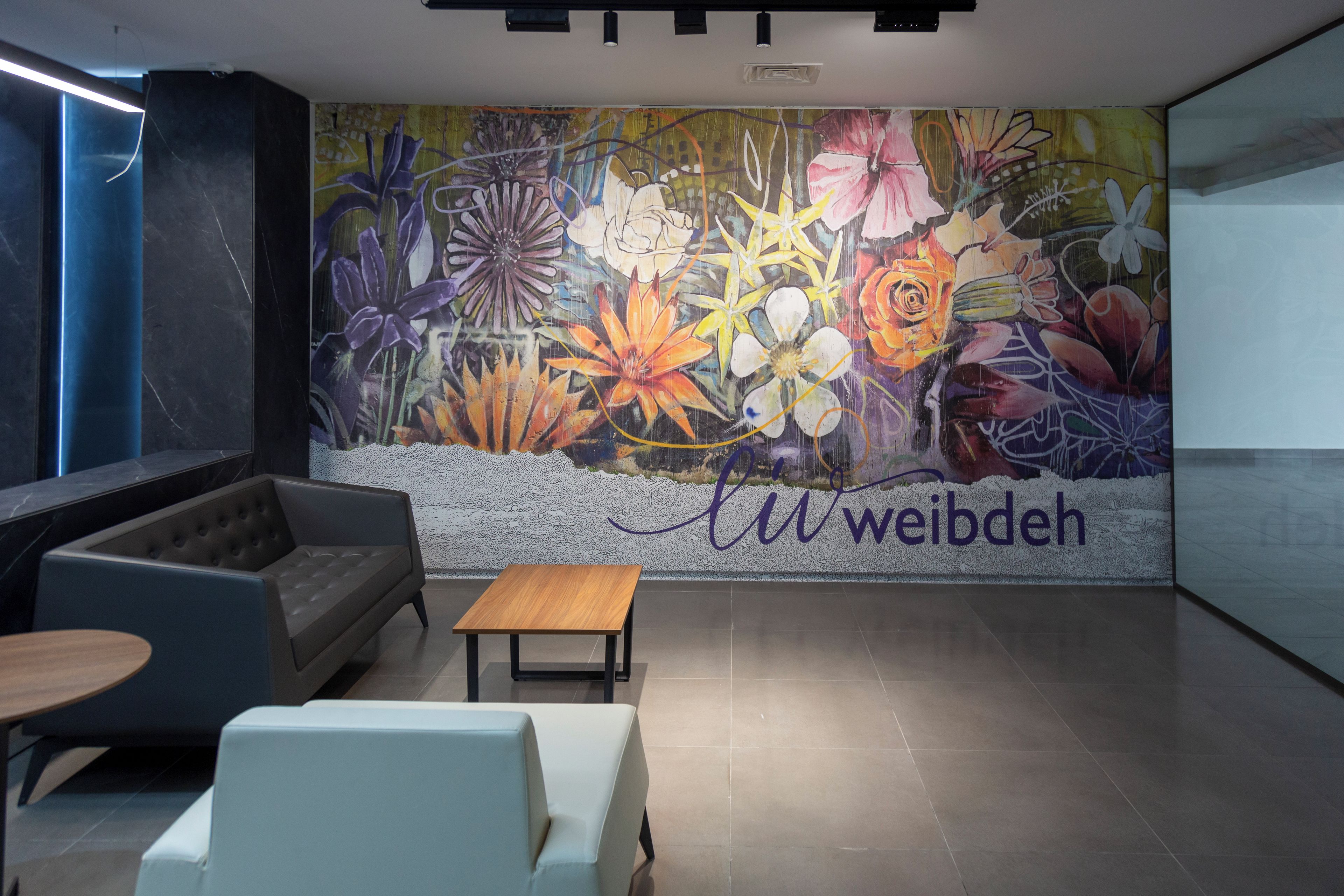 A modern lobby with a floral mural, a sofa, a wooden table, and a white chair.
