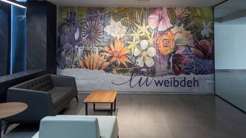 A modern lobby with a floral mural, a sofa, a wooden table, and a white chair.