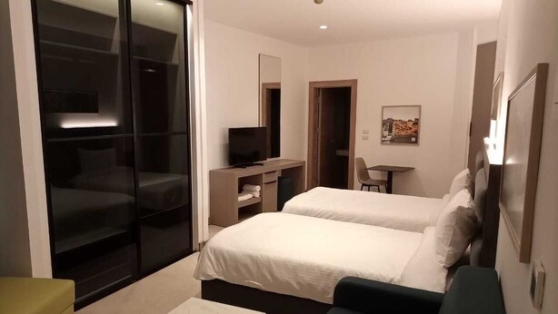 Une chambre d’hôtel moderne équipée de deux lits, d’un bureau, d’une chaise et d’une porte-fenêtre coulissante donnant sur un balcon.