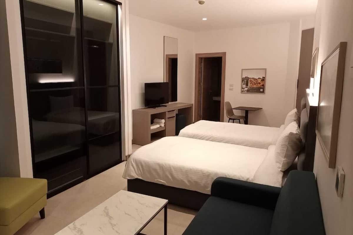 Moderni hotellihuone, jossa on kaksi sänkyä, työpöytä, tuoli ja liukuovet, jotka johtavat parvekkeelle.