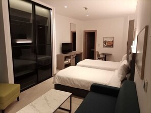 Une chambre d’hôtel moderne équipée de deux lits, d’un bureau, d’une chaise et d’une porte-fenêtre coulissante donnant sur un balcon.