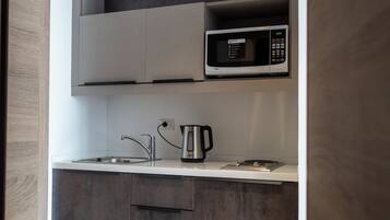 A modern kitchen with grey cabinets, a microwave, a kettle, and a sink.