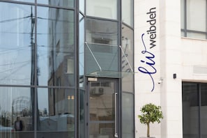 Un edificio con grandes ventanales que reflejan el entorno, un cielo despejado y un letrero con el nombre "li weibdeh".