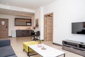 Un salon moderne comprenant un canapé, une table basse avec une plante, un téléviseur et un coin cuisine avec des placards et un four à micro-ondes.