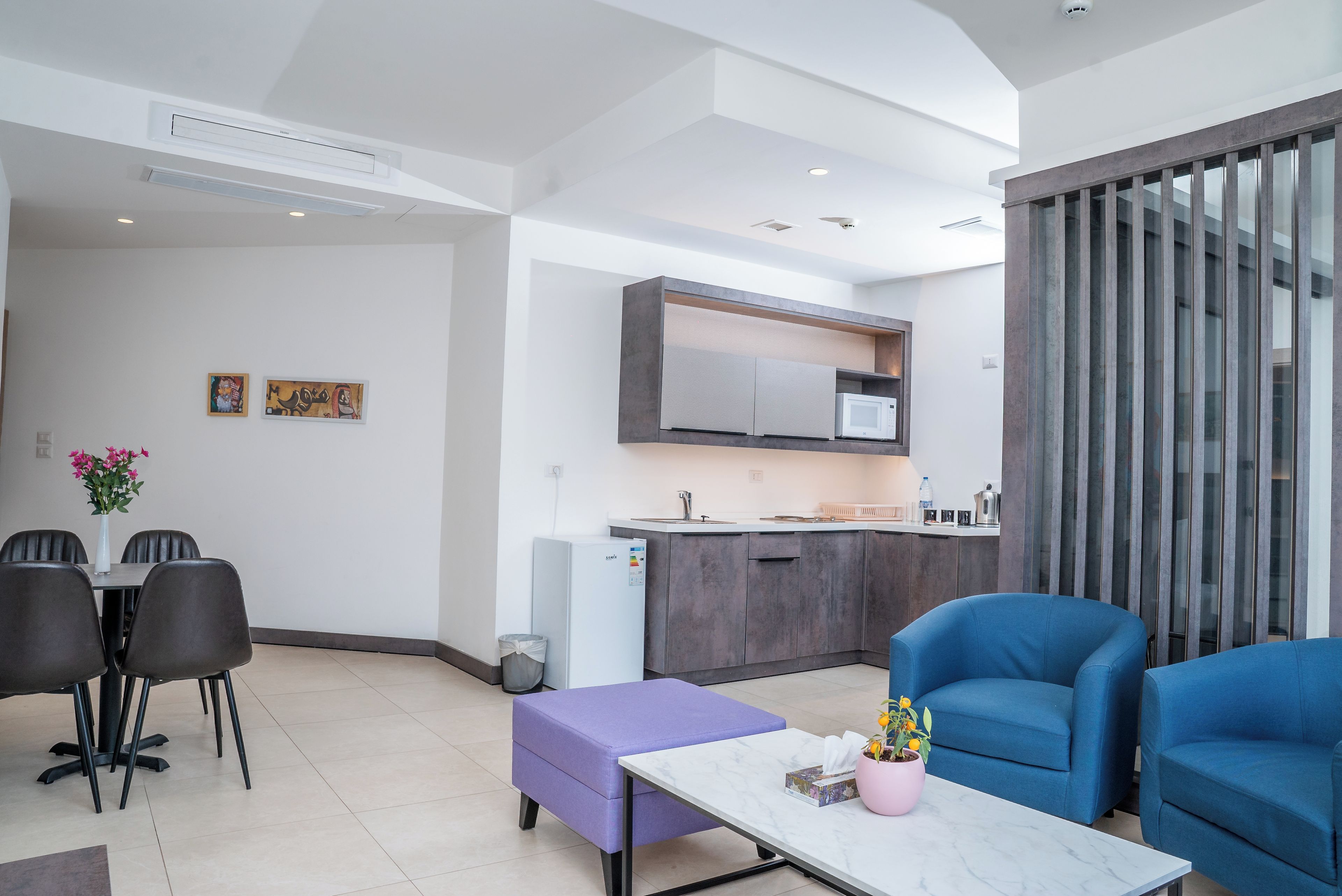 A modern living area with a dining table, chairs, a purple ottoman, and blue armchairs.
