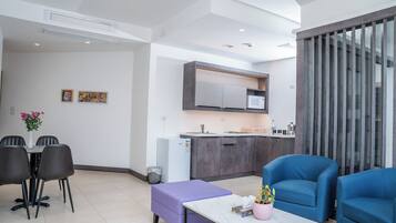 A modern living area with a dining table, chairs, a purple ottoman, and blue armchairs.