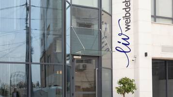 A building with large glass windows reflecting the surroundings, a clear sky, and a sign with the name "li weibdeh".