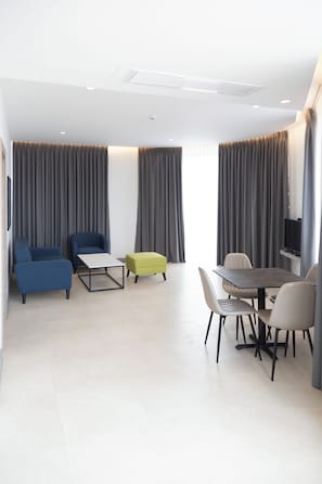 A modern hotel room with a dining area, two sofas, a small table, and a TV mounted on the wall. - Liv Weibdeh Hotel Suites (Amman)