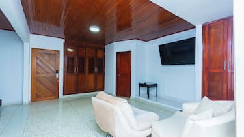 A spacious room with a wooden ceiling, a flat-screen TV mounted on the wall, and two cream-colored sofas.