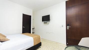 A hotel room with a bed, a television mounted on the wall, a door, and a small table.