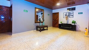 A lobby with a wooden ceiling, a mirror, a console table with vases, a fire extinguisher, and directional signs. - Suite 94 Hotel Baq (Barranquilla)