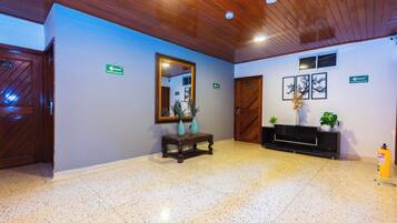 A lobby with a wooden ceiling, a mirror, a console table with vases, a fire extinguisher, and directional signs.