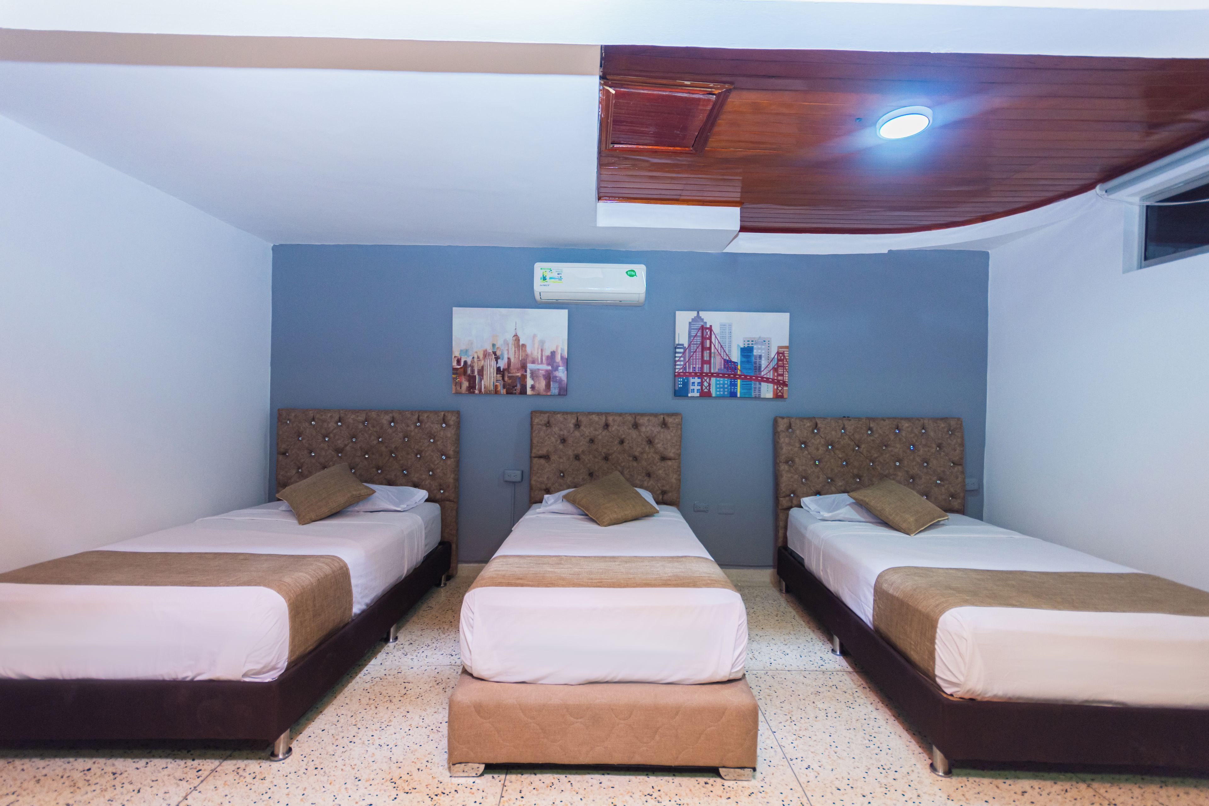 Une chambre d’hôtel avec trois lits, un ventilateur de plafond et deux climatiseurs fixés au mur.