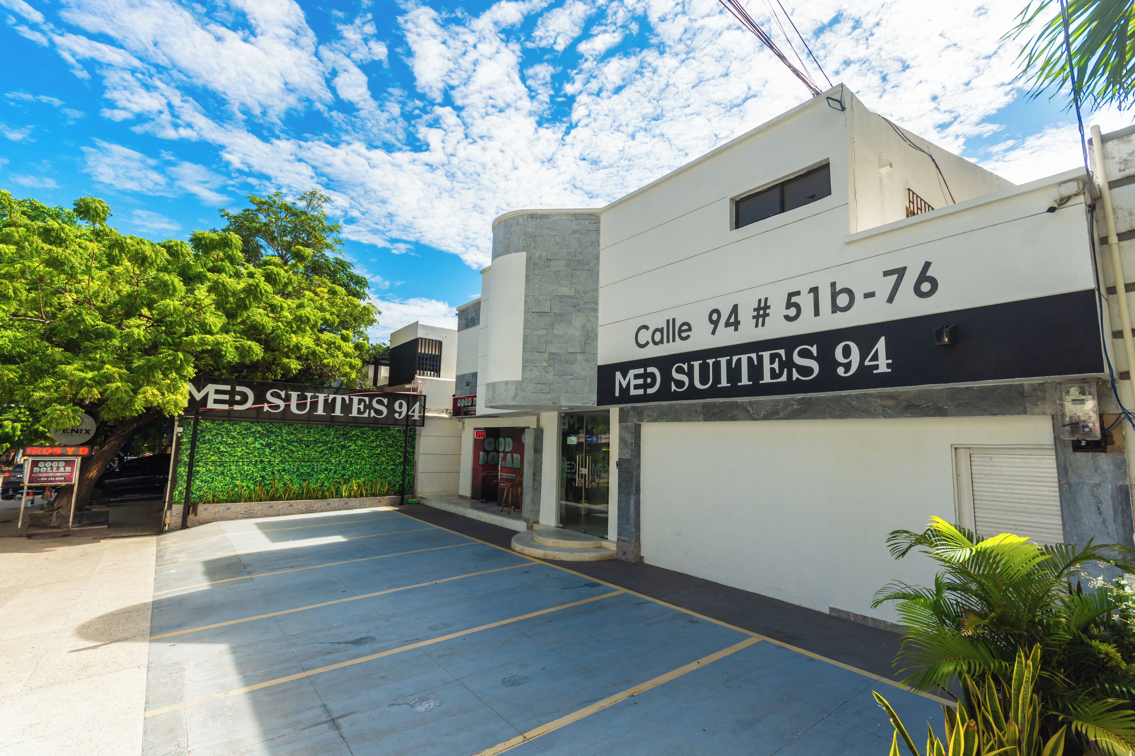 A building with a sign reading "Calle 94 # 51b-76 MED SUITES 94" and a parking lot in front.