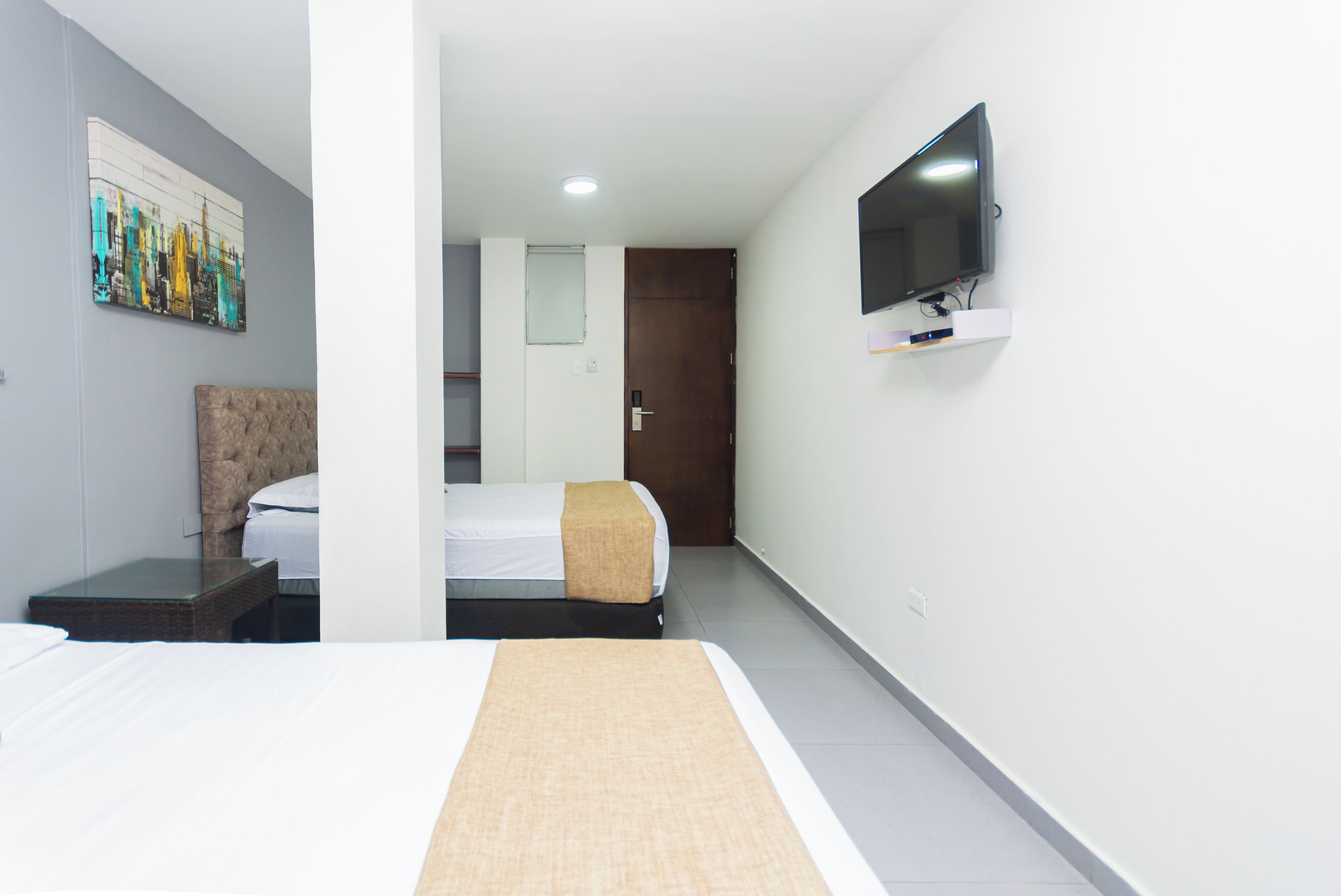 A hotel room with a bed, a TV mounted on the wall, and a painting on the wall.
