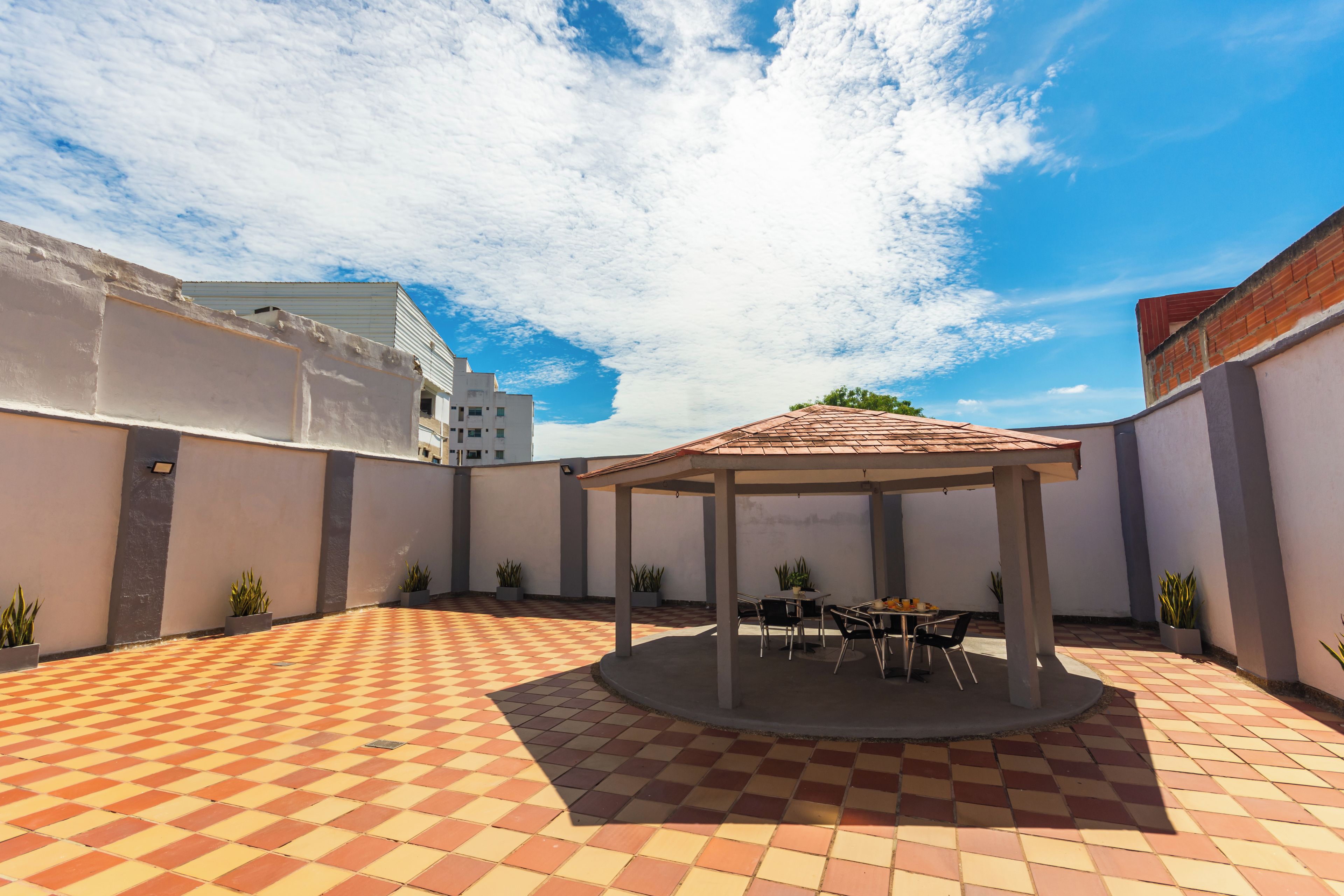 A courtyard with a checkered floor, a covered seating area, and potted plants.