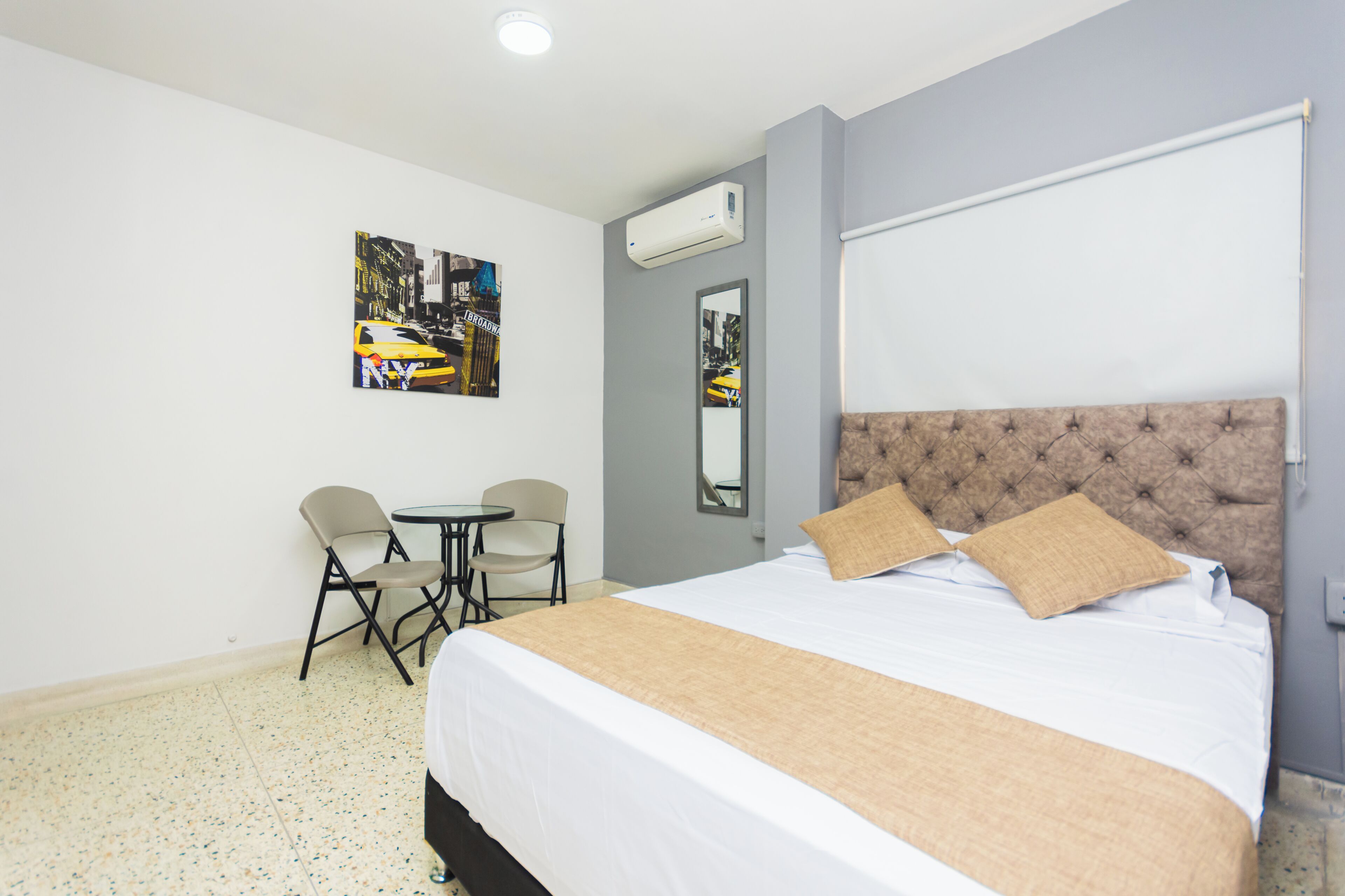 Habitación de hotel con una cama grande, una mesita pequeña, dos sillas y un aire acondicionado instalado en la pared.