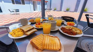 A breakfast setting with plates of scrambled eggs, toast, and fruit, along with orange juice and coffee.