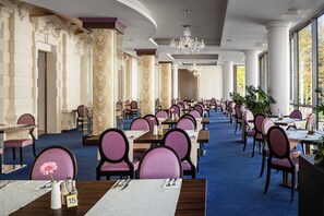 A spacious dining area with rows of tables and chairs, large windows, and decorative columns. - Grandhotel Nabokov Spa & Wellness (Marianske Lazne)