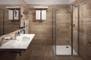 A modern bathroom with a glass-enclosed shower, a white sink, and marble-patterned walls. - Grandhotel Nabokov Spa & Wellness (Marianske Lazne)