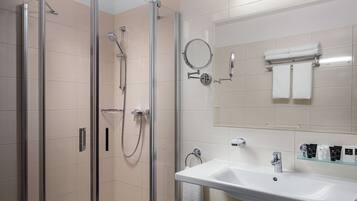 Un baño moderno con ducha de vidrio, lavamanos con espejo y artículos de aseo ordenados.