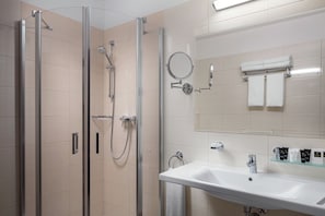 A modern bathroom with a glass-enclosed shower, a sink with a mirror, and neatly arranged toiletries. - Grandhotel Nabokov Spa & Wellness (Marianske Lazne)