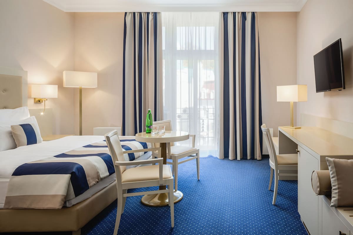 A hotel room with a bed, a desk, a chair, a TV, and a window with curtains.