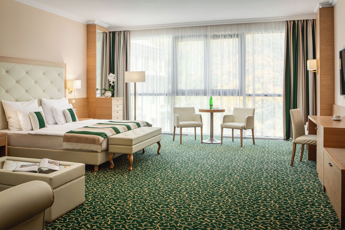 A hotel room with a large bed, a sitting area with chairs, a small table, and a desk.