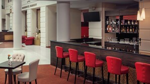 A modern bar area with red bar stools, a black countertop, and a television mounted above the bar. - Grandhotel Nabokov Spa & Wellness (Marianske Lazne)