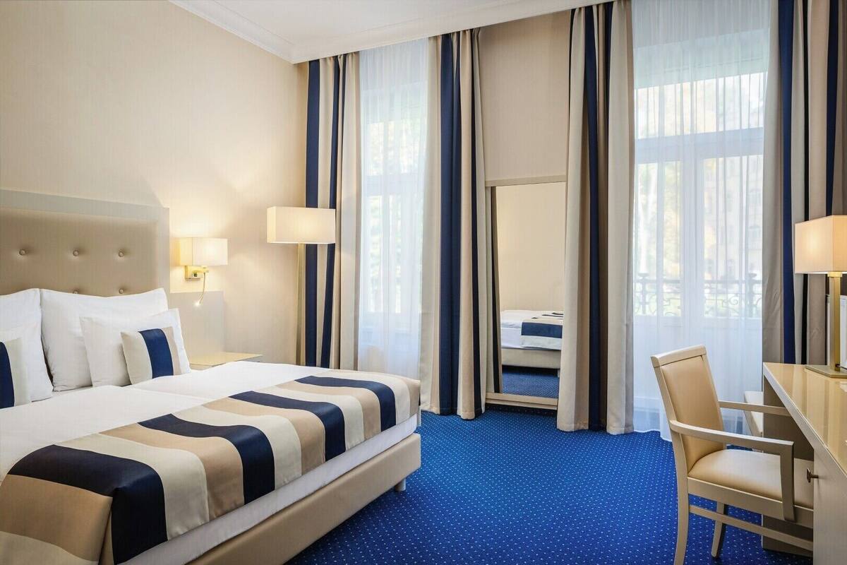 A hotel room with a large bed, a desk, and a chair. There are curtains and a window with a view.