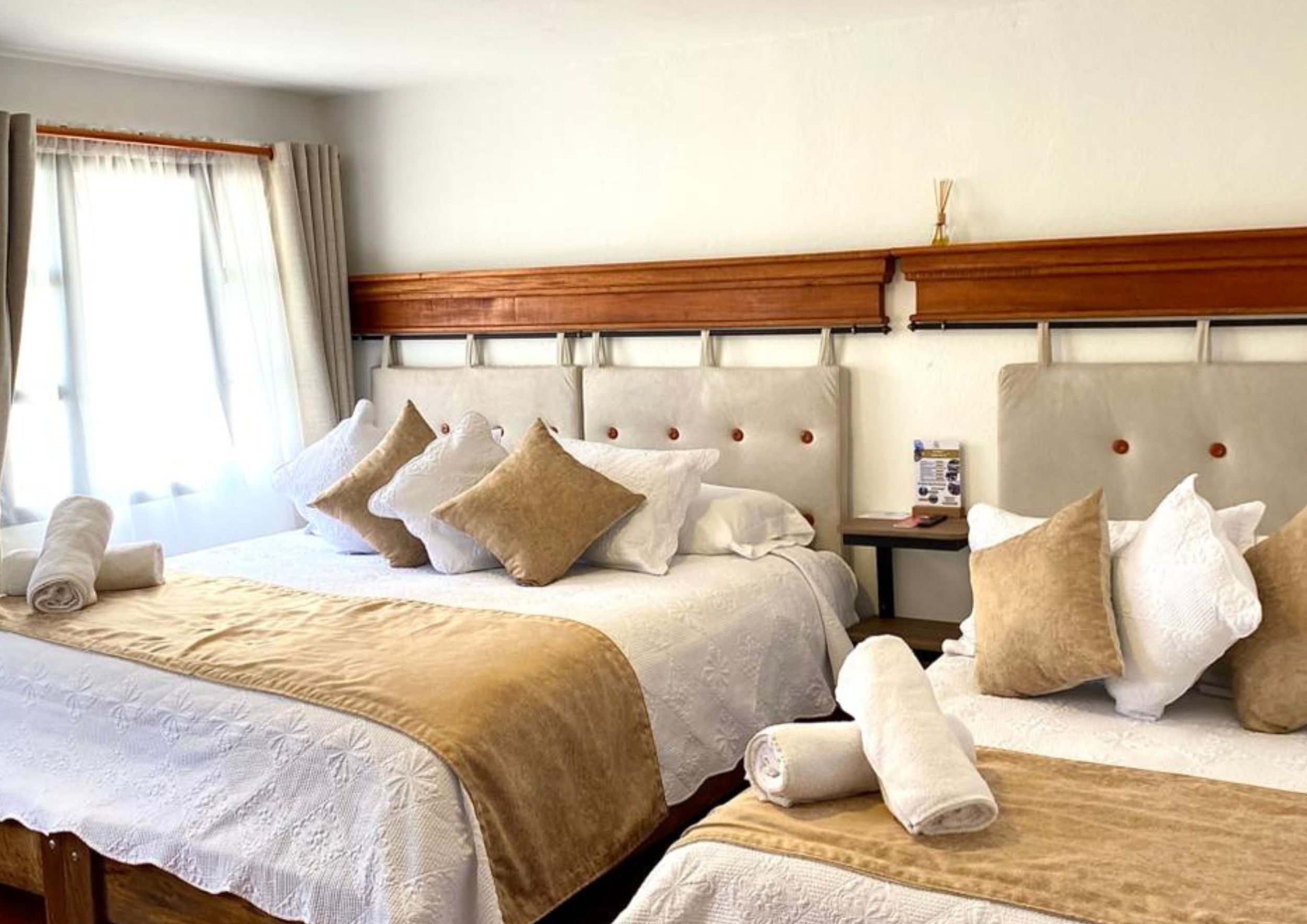 A hotel room with two beds, each with a wooden headboard, white linens, and beige throw blankets.