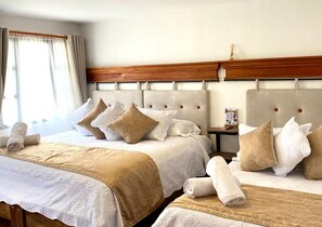 A hotel room with two beds, each with a wooden headboard, white linens, and beige throw blankets. - Hotel Calle Real (Villa de Leyva)