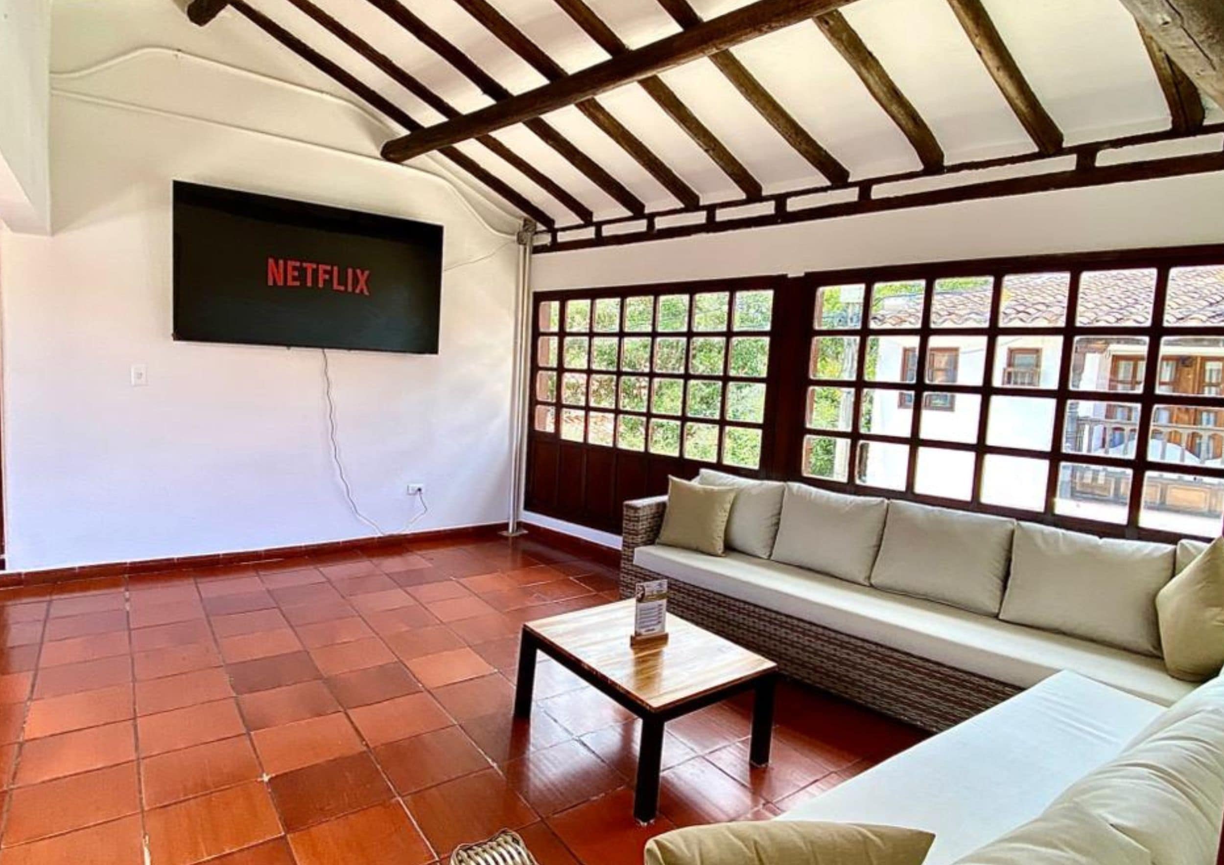 Una sala de estar con un televisor montado en la pared, un sofá, una mesa de centro y un ventanal con vistas a edificios.
