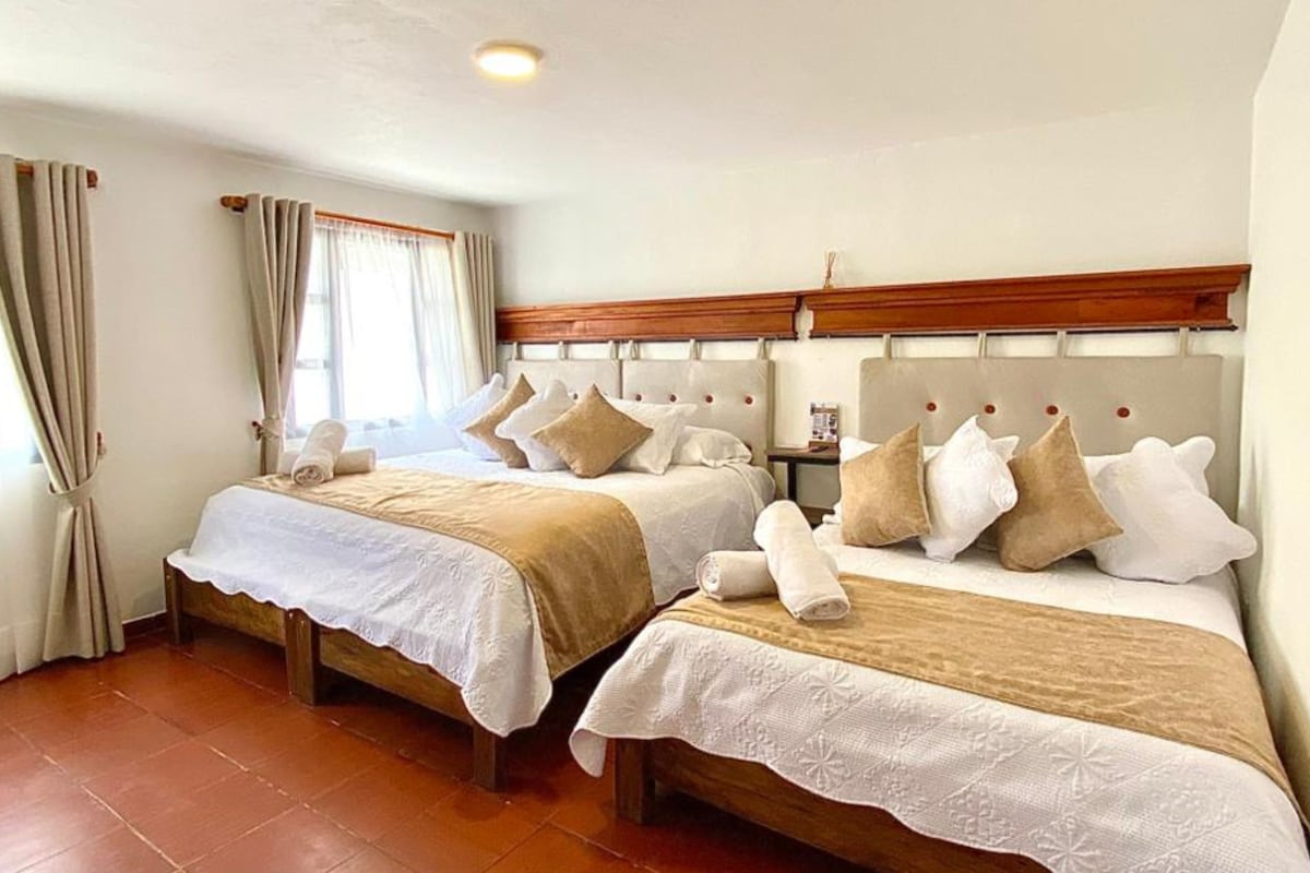A hotel room with two beds, each with a wooden headboard, white linens, and multiple pillows.