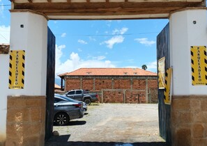 A gated entrance with a brick building in the background, a gravel driveway, and parked cars. - Hotel Calle Real (Villa de Leyva)