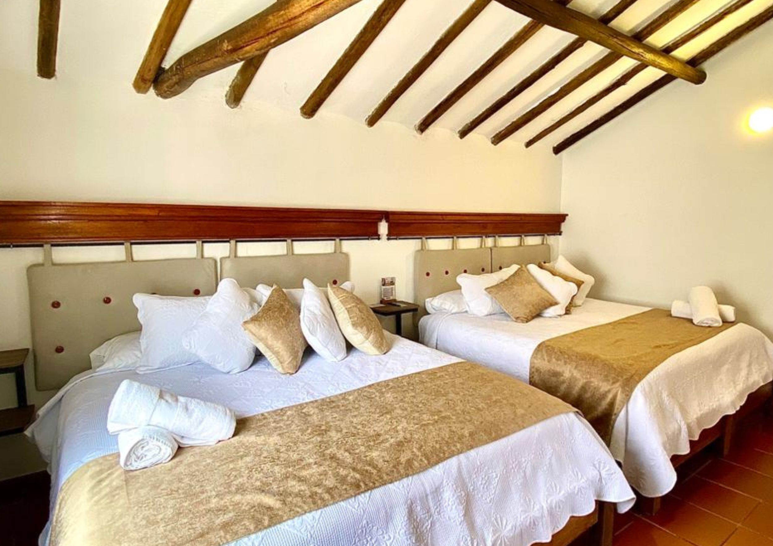 Habitación de hotel con dos camas, cabecero de madera, ropa de cama blanca y suelo de baldosas.