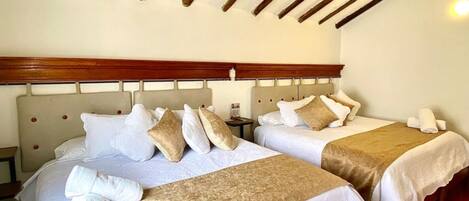 Habitación de hotel con dos camas, cabecero de madera, ropa de cama blanca y suelo de baldosas.