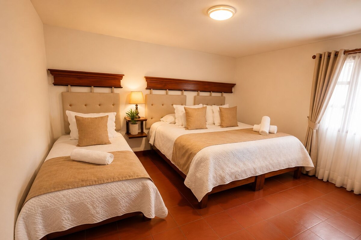 Une chambre d’hôtel avec deux lits, une table de chevet avec une lampe et une fenêtre avec des rideaux.