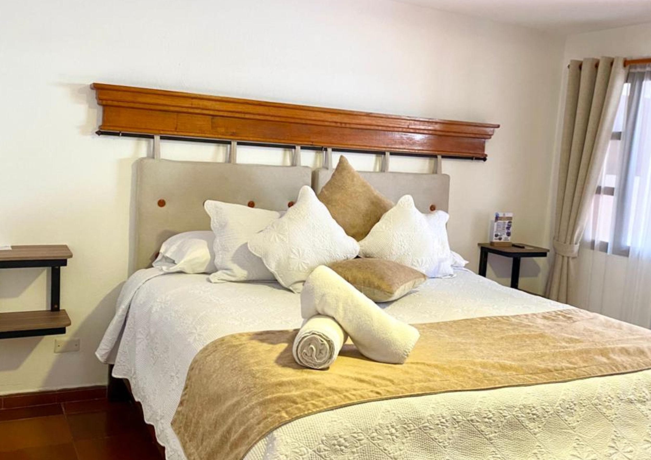 A neatly made bed with a headboard, pillows, and a rolled-up blanket.