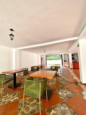 A spacious indoor area with multiple tables and chairs, a reception desk, and a view of greenery outside. - Hotel Calle Real (Villa de Leyva)