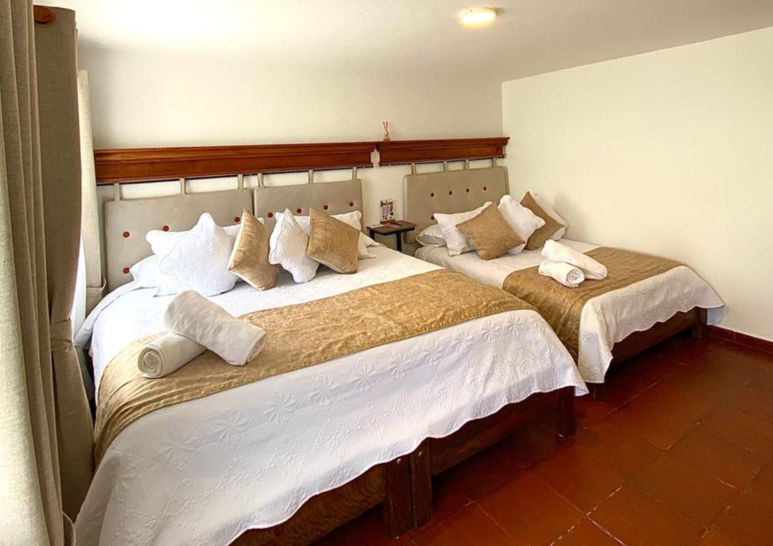 A hotel room with two beds, a wooden headboard, a small bedside table, and a tiled floor.