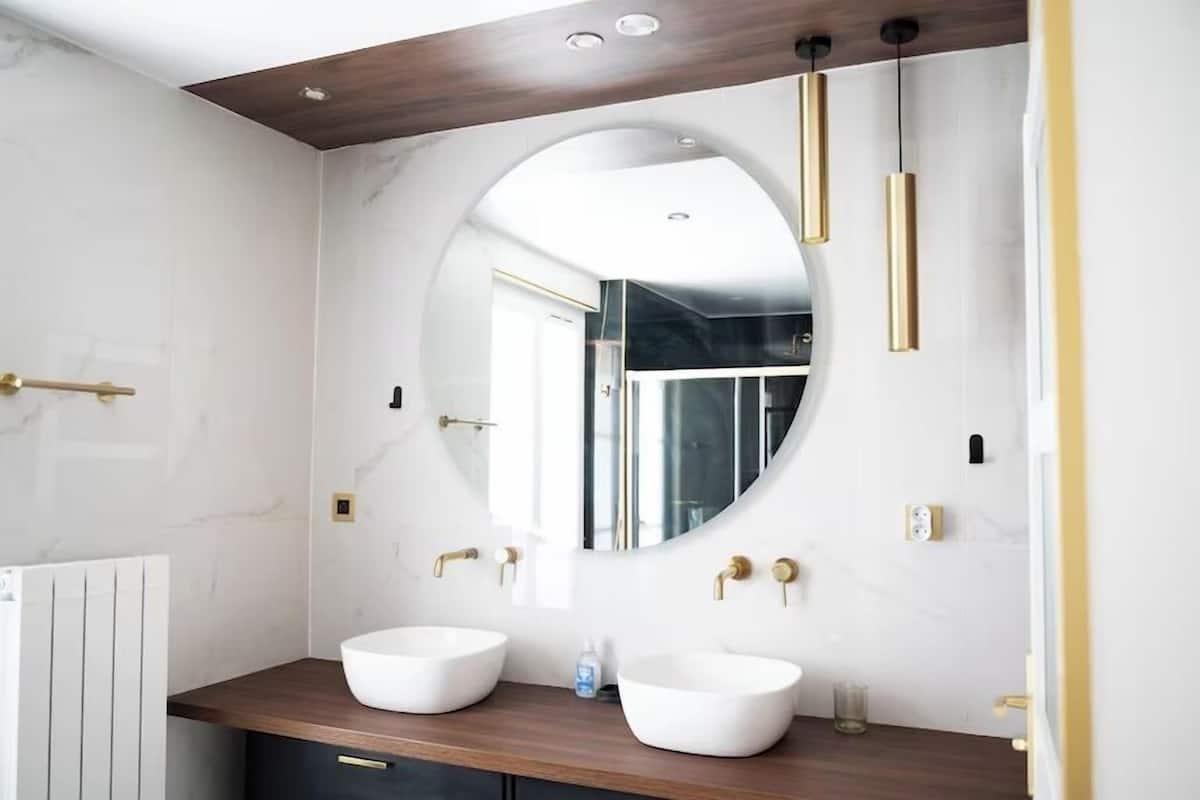 A modern bathroom with two white sinks, a large mirror, and gold fixtures.