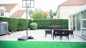 A backyard with a basketball hoop, a patio table with chairs, and a large window. - Villa Alexandre Dumas (Bussy-Saint-Georges)
