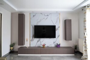 Un soggiorno moderno con una grande televisione a schermo piatto montata su una parete in marmo, un mobile porta TV scuro sotto e una piccola pianta sul pavimento.