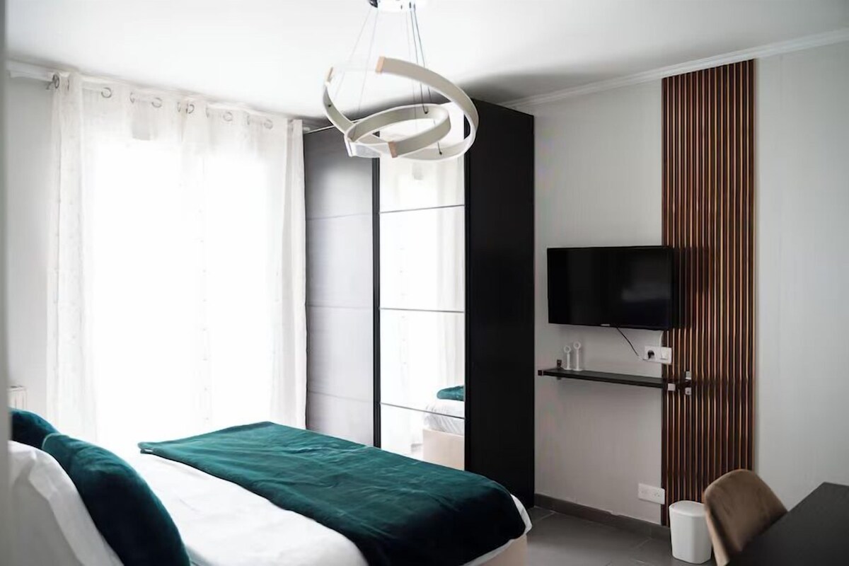 Ein Hotelzimmer mit Bett, Fernseher, Fenster mit Vorhängen und einer Wand aus Holzverkleidung.