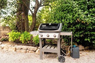 Una parrilla portátil para barbacoa con panel de control, tanque de combustible y rueda para facilitar su transporte.